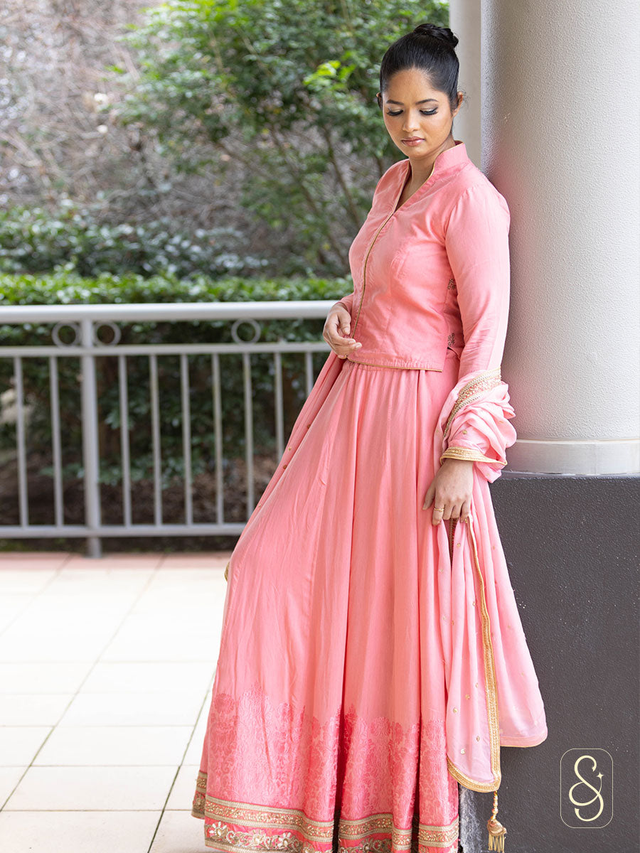 Woman in a pink traditional outfit with golden border standing outdoors.