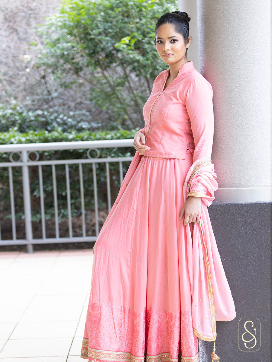 Woman in a soft pink silk traditional lehenga standing outdoors.