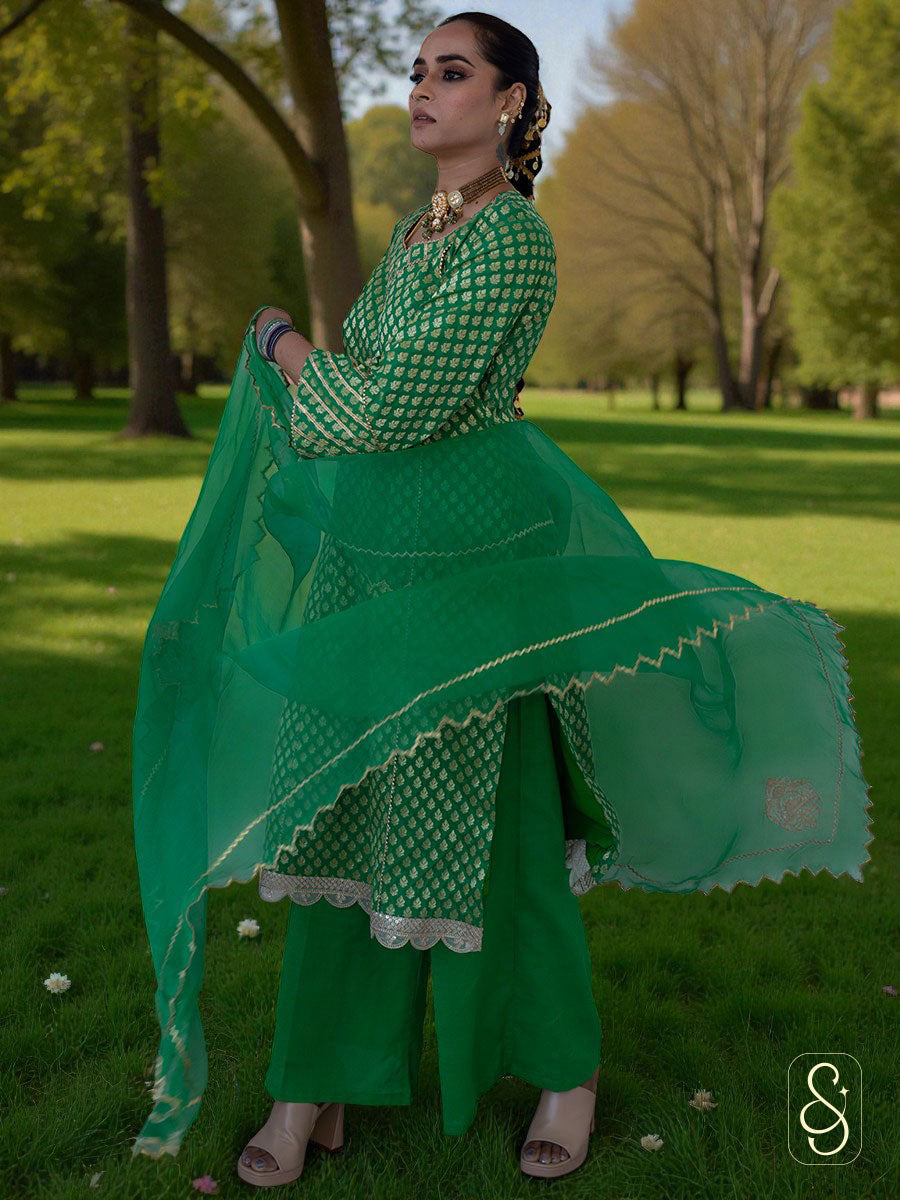 Woman in a green traditional outfit with gold patterns, standing against a white background.