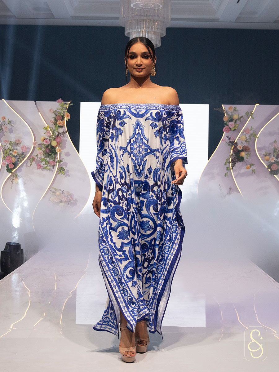 Model wearing a blue and white patterned kaftan on a fashion show runway.