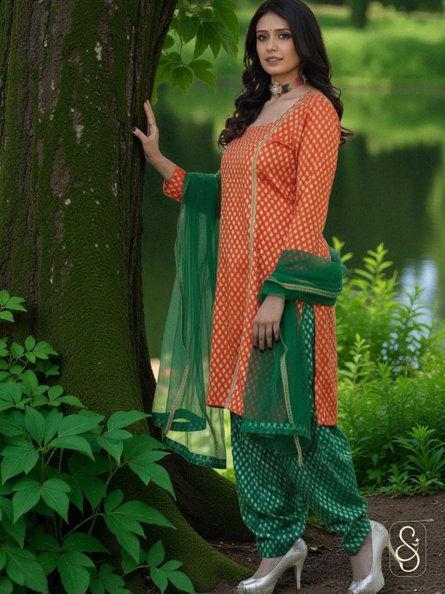 Woman in an orange and green traditional salwar standing next to a tree in a garden.