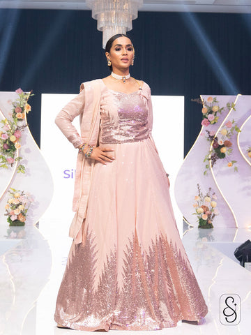Woman in a pastel pink sequin work lehenga and full sleeve blouse with georgette dupatta, posing on a ramp stage.
