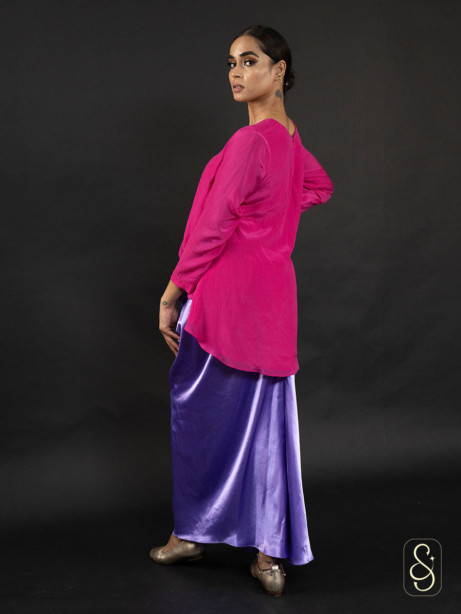 Woman showing her bright pink top and purple skirt from back.