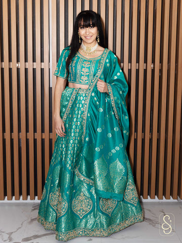 Woman wearing a teal embroidered banarasi lehenga against a wooden panel background