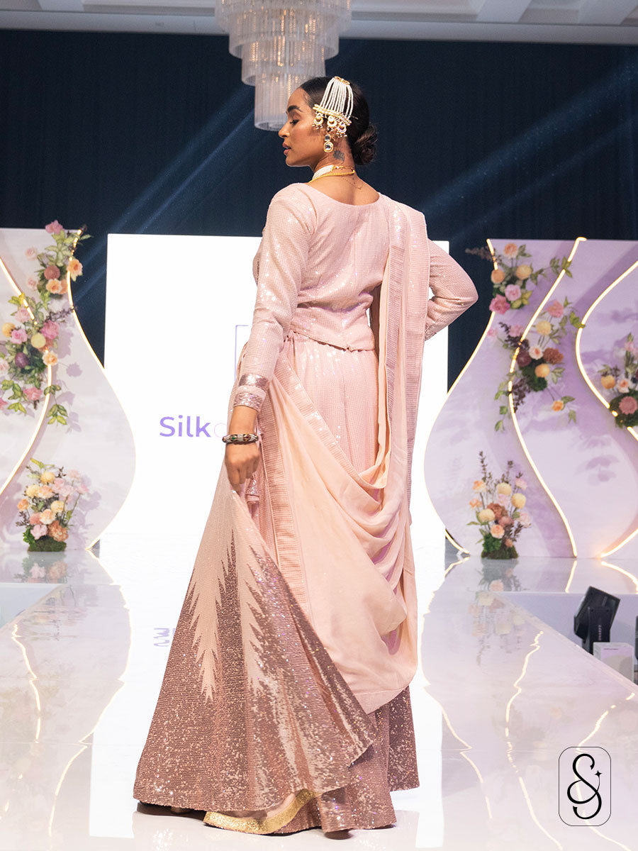 Back view of a woman wearing a pastel pink sequin work lehenga with matching georgette dupatta and full sleeve blouse, along with statement jewellery.