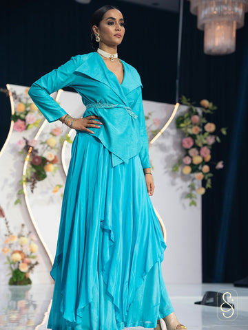 Woman in a turquoise coloured asymmetrical, flared crepe skirt posing on a stage with floral decorations.