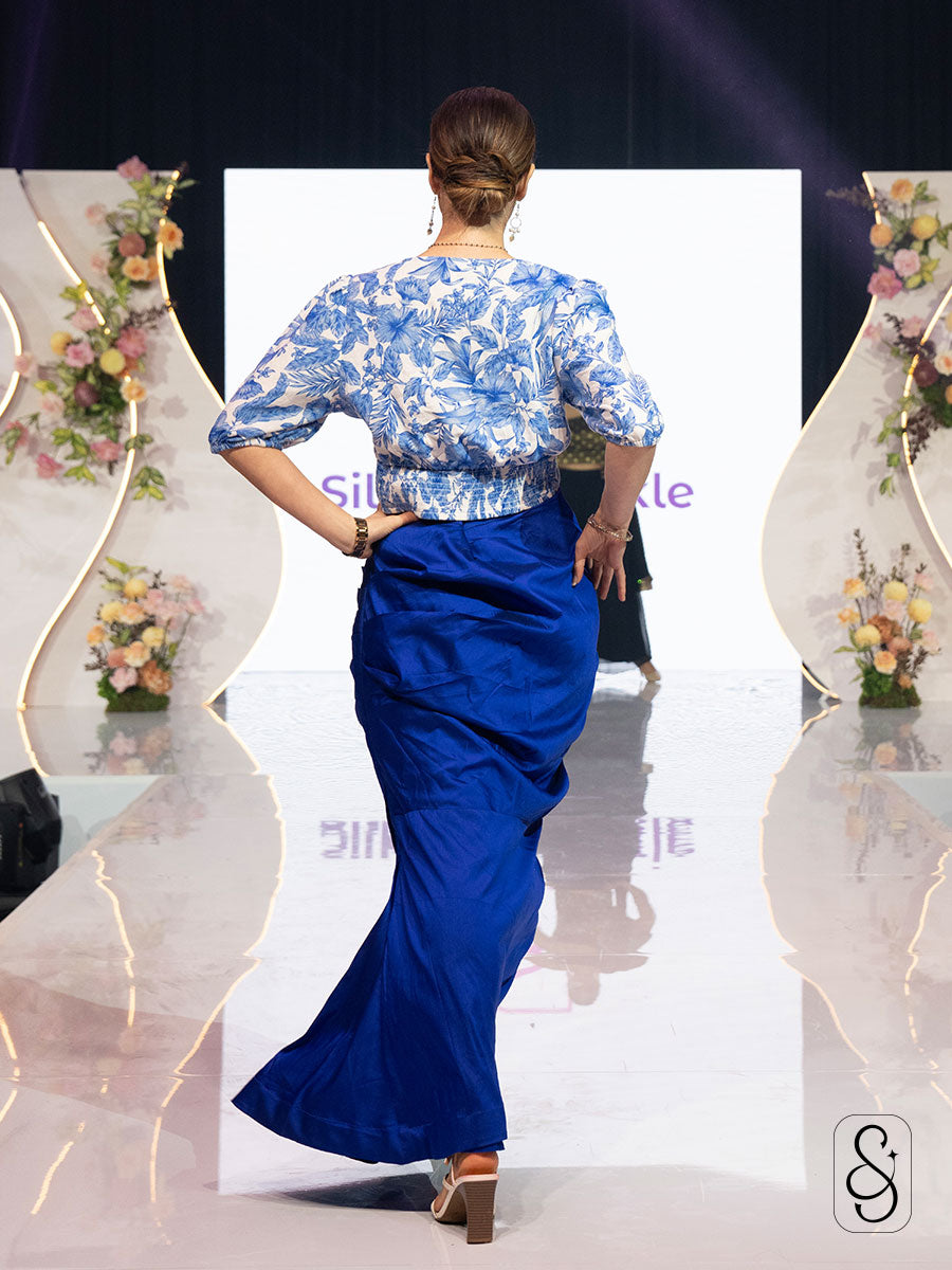 Back view of a model wearing a blue floral top and skirt on a runway.