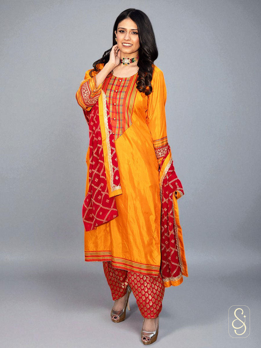 Woman wearing a traditional orange and red suit with a matching dupatta on a gray background