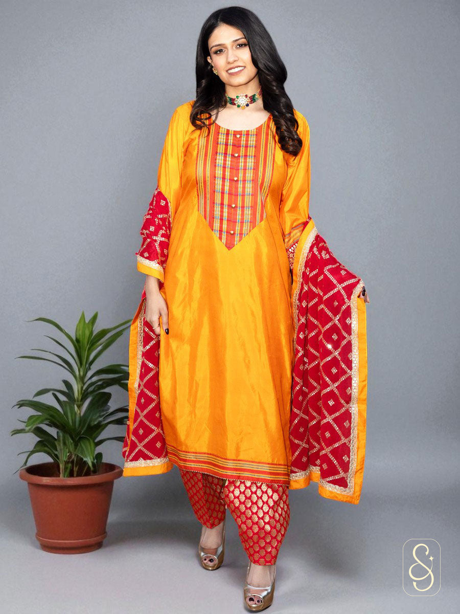 Woman wearing a traditional orange and red suit with a matching dupatta on a gray background