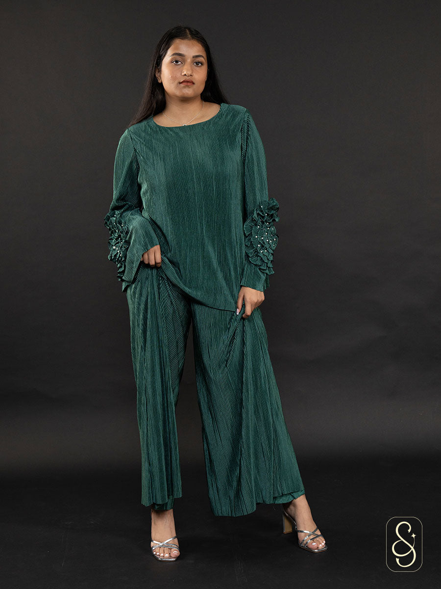 Woman posing by wearing a green co-ord set with embellished sleeve design on a dark background.