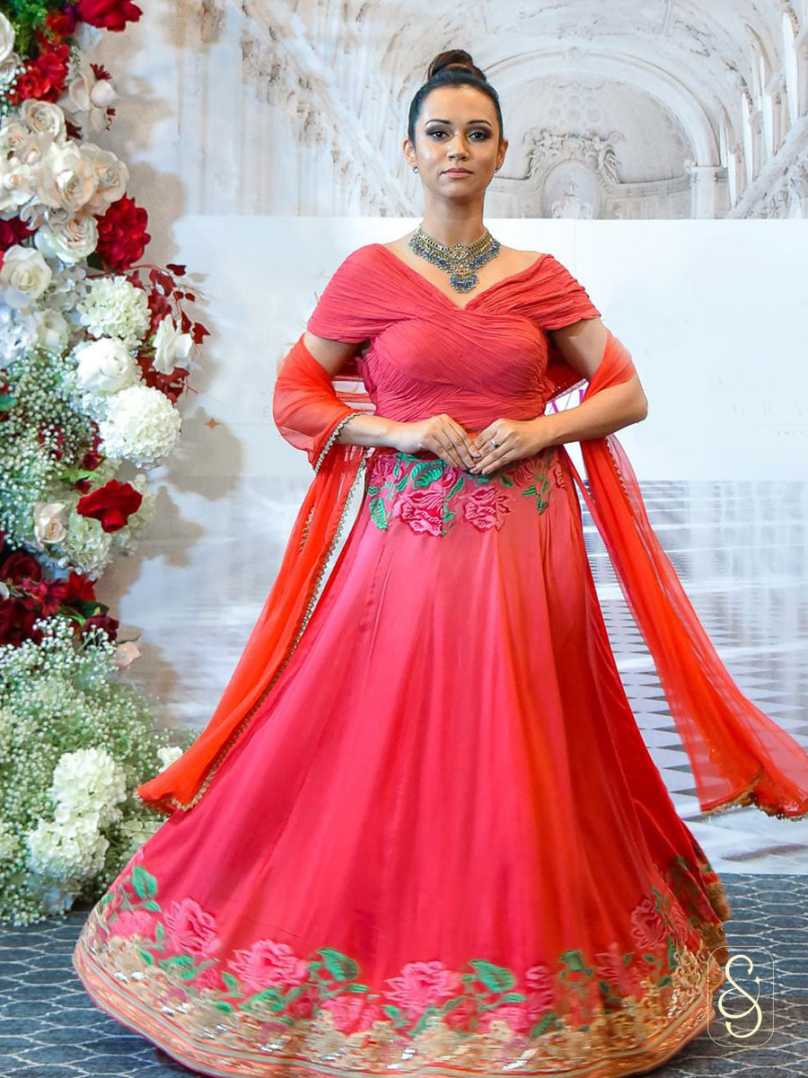 A woman in a soft silk floral embroidered red coloured lehenga with matching ruched blouse and net dupatta. 